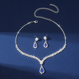 Close-up of silver necklace and earrings set with blue teardrop crystals on dark blue background