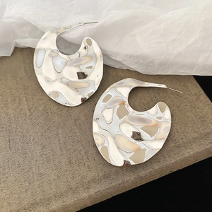 Macro detail of large irregular silver earrings with wavy texture on minimalist display