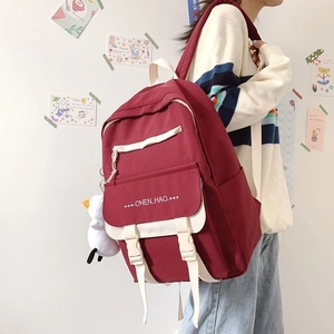Detail of wine red canvas backpack with white buckle straps and cute penguin plush charm