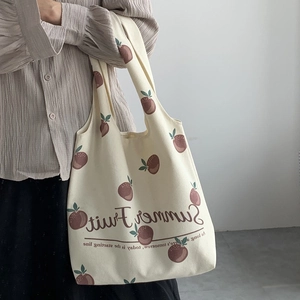 Off-white canvas tote bag with red fruit print shown in a stylish over-the-shoulder view