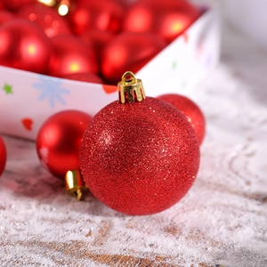 Red Christmas tree ornaments set with glitter and glossy finish on snowy wood surface