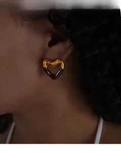 Detail of heart stud earrings in gold and brown enamel on model ear