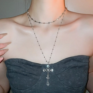 Close-up of layered silver cross necklace with crystal pendant worn by a model