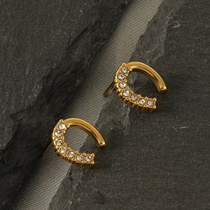 Boucles d'oreilles en forme de C dorées avec strass sur une surface en ardoise