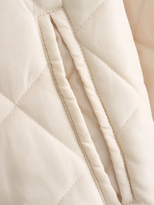 Gros plan du tissu matelassé en losanges et poche latérale sur la veste beige