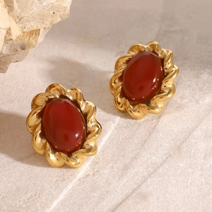 Nahaufnahme vintage Ohrstecker mit rotem Achat und goldener Wellentextur auf Marmor