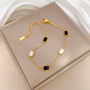 Titanium steel gold bracelet with black and white rectangle charms on silk background
