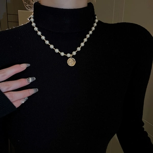 Nahaufnahme der Perlenkette mit Goldmünzen-Porträtanhänger auf schwarzem Pullover