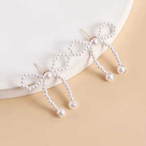 Detail of handcrafted white pearl bow earrings on a white stone display stand