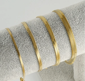 Flat gold snake blade chains in four different widths displayed on a jewelry stand