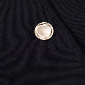 Close-up of golden metallic button detail on dark twill fabric jacket and shorts set
