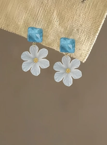 Detailed macro view of elegant blue and white acrylic flower earrings with golden core accents.
