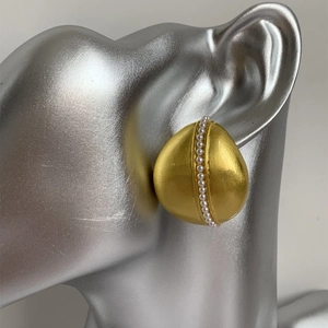 Dettaglio macro di orecchini vintage in oro opaco con perle su modella elegante