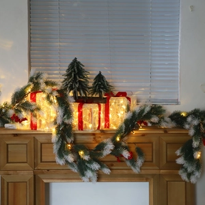 Lighted Christmas pine garland with snow effect and glowing gift boxes on mantelpiece