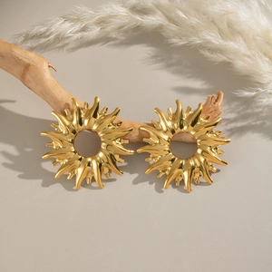 Detail of golden sun-shaped titanium earrings on a branch with reed background