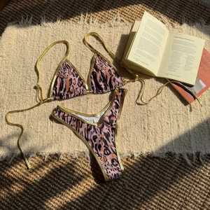 Flat lay of leopard print bikini with gold metallic straps on rustic woven fabric background