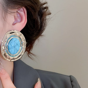 Dettaglio di orecchini vintage dorati con pietre ovali in acrilico turchese su modella