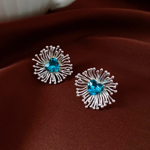 Macro shot of silver flower earrings with teal heart zircon on dark silk background