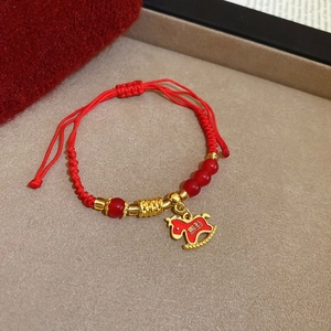 Dettaglio macro del braccialetto intrecciato rosso con ciondolo a cavallo e perle rosse