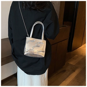 Close-up of silver metallic handbag with bow detail and chain strap on a model