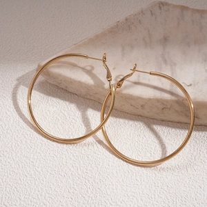 Detail of large gold hoop earrings resting on marble stone with soft shadows