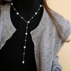 Close-up of elegant Y-shaped pearl long necklace styled over a black turtleneck sweater