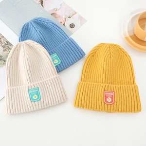 Detailed flat lay of knitted beanies in blue, beige, and yellow with woven brand labels