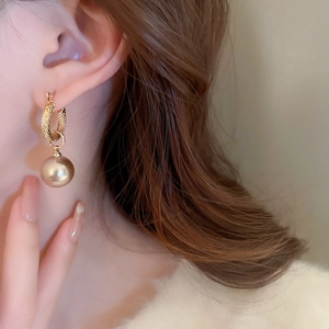 Primer plano de pendiente de aro trenzado dorado con perla grande color champán en modelo