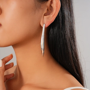 Gros plan d'une boucle d'oreille barre courbée en argent portée sur l'oreille d'un modèle