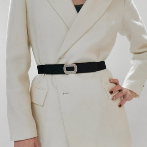 Elastic black waist belt with a rectangular rhinestone buckle on a white blazer