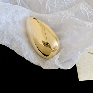 Macro detail of a high-polished golden sun leaf brooch on a white textured background