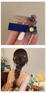Dettaglio di due fermagli per capelli con fiori blu e pietre preziose sulla treccia