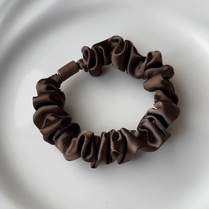 Macro detail of dark brown satin scrunchie with silk luster and accordion pleat texture