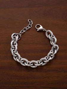 Detail of silver chain bracelet with lobster clasp and textured links on wood background