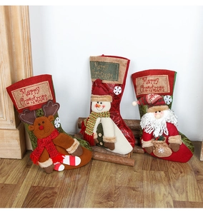 Three plush Christmas stockings with Santa, snowman and reindeer figures on wood floor