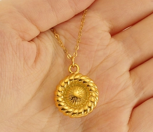 Gros plan du collier en acier inoxydable doré avec pendentif soleil et texture gravée
