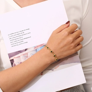 Detail of a gold stainless steel bracelet featuring a black heart charm on a female wrist