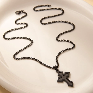 Detalle de un collar de cruz gótica en negro mate sobre un plato de cerámica blanca