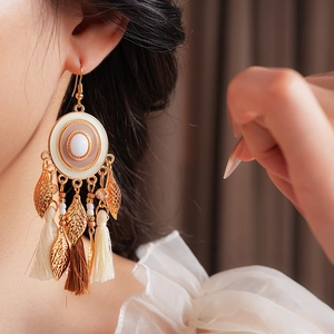 Detail of bohemian drop earrings with white stone, golden leaves and silk tassels