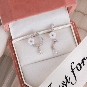 Macro detail of asymmetric shell flower earrings with colorful zircons in a pink velvet box