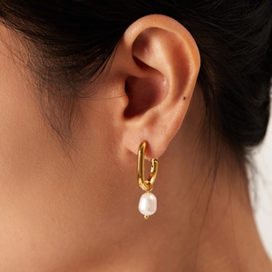 Macro view of gold oval hoop earring with a natural baroque pearl pendant for women