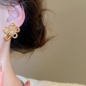 Close-up of a gold hollow flower earring with sparkling crystals on a female ear
