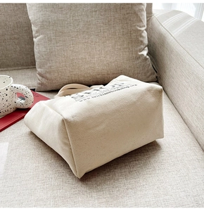 Close-up of beige canvas tote bag with black text placed on a soft sofa setting