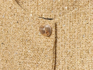 Dettaglio macro del tessuto tweed oro champagne e bottone metallico con goffratura