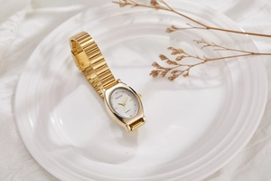 Detailed macro view of vintage oval gold watch with wave textured strap on white fabric