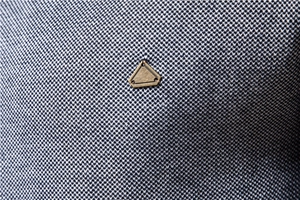 Close-up of dark blue knit fabric featuring a bronze metal triangle logo detail