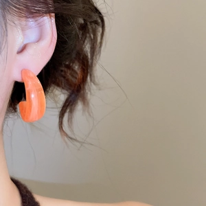 Close-up of elegant orange acrylic C-shaped hoop earrings worn by a model for a chic look