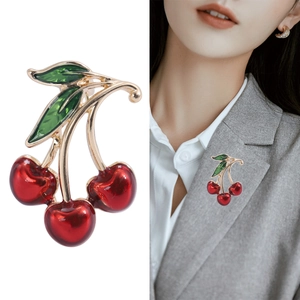 Elegant red cherry brooch with green leaves and gold stem shown on suit lapel