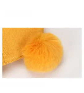 Détail du bonnet tricoté pour bébé avec maille fine jaune et pompon en fourrure douce