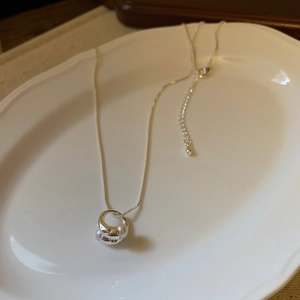 Vista dettagliata della collana argento con ciondolo di perle su un piatto bianco